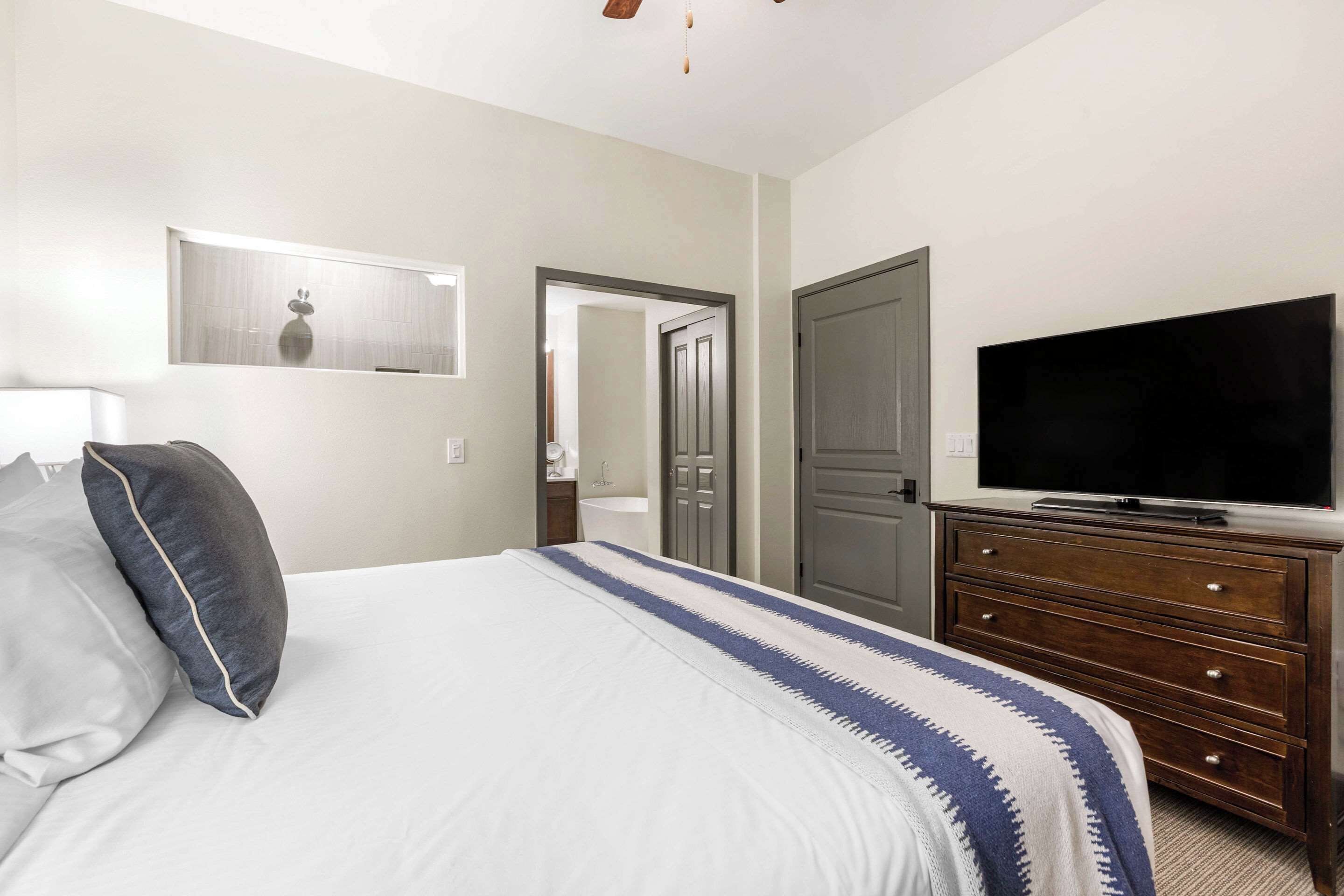 Habitación de hotel con cama, televisor, cómoda y puerta que da a otra habitación.