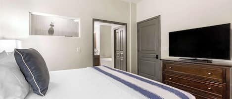 Habitación de hotel con cama, televisor, cómoda y puerta que da a otra habitación.