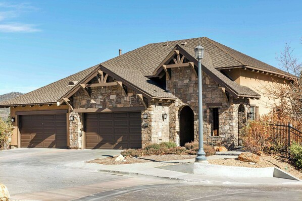 Une maison à deux étages avec une façade en pierre, deux portes de garage et un jardin paysager à l’avant.
