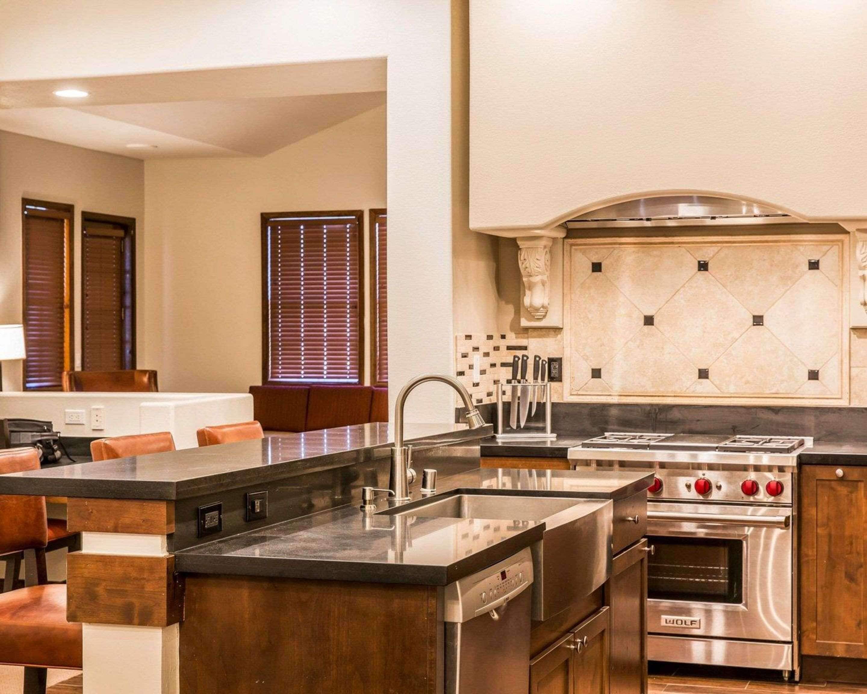 A modern kitchen with a central island, stainless steel appliances, and a seating area with brown leather chairs.