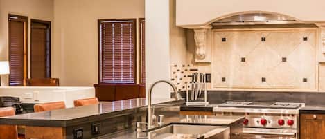 A modern kitchen with a central island, stainless steel appliances, and a seating area with brown leather chairs.