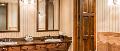 Un baño con dos lavamanos, una bañera grande, armarios de madera y paredes con espejos.