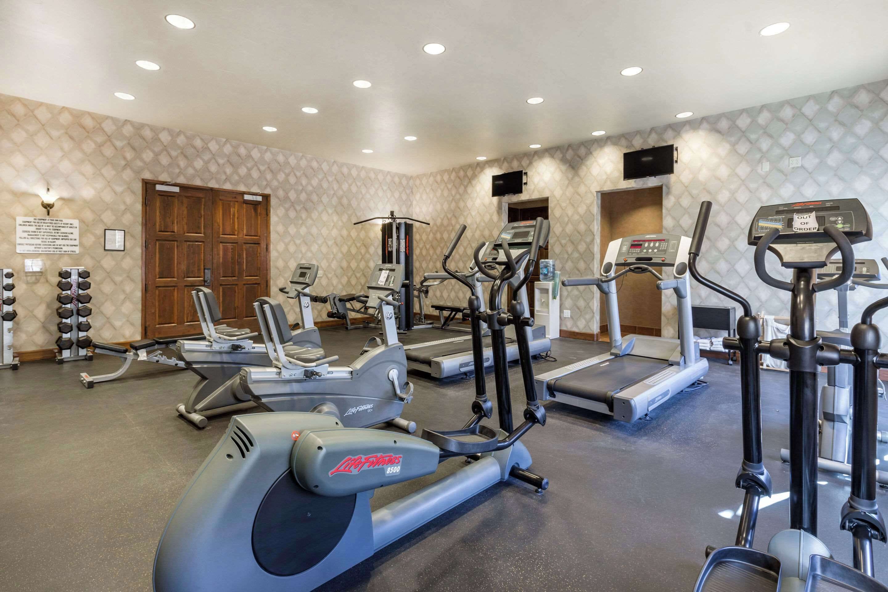 A gym with various cardio machines, a weight rack, and a wooden door.