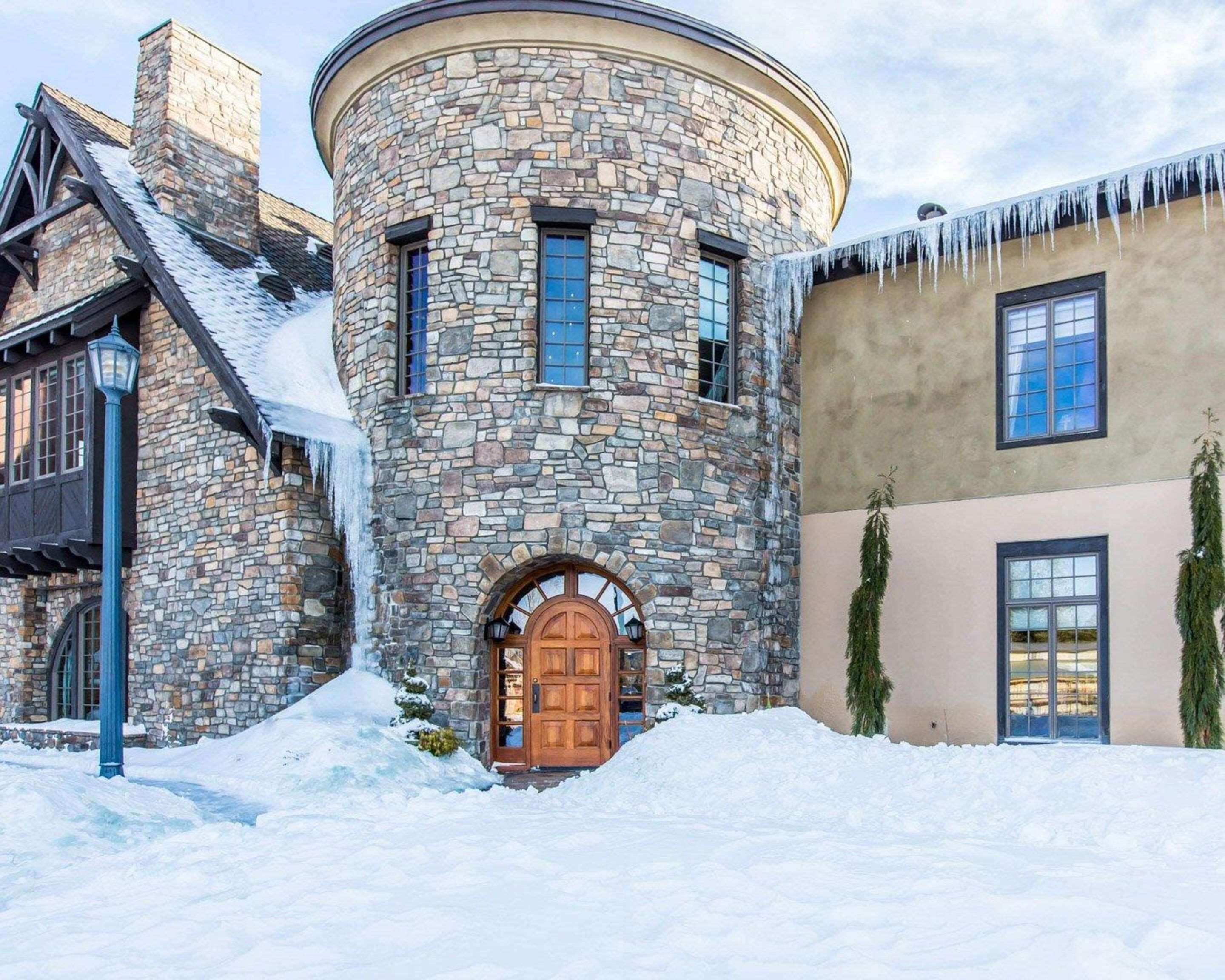 Un edificio de piedra con una torre redonda, una puerta de madera y un paisaje cubierto de nieve.