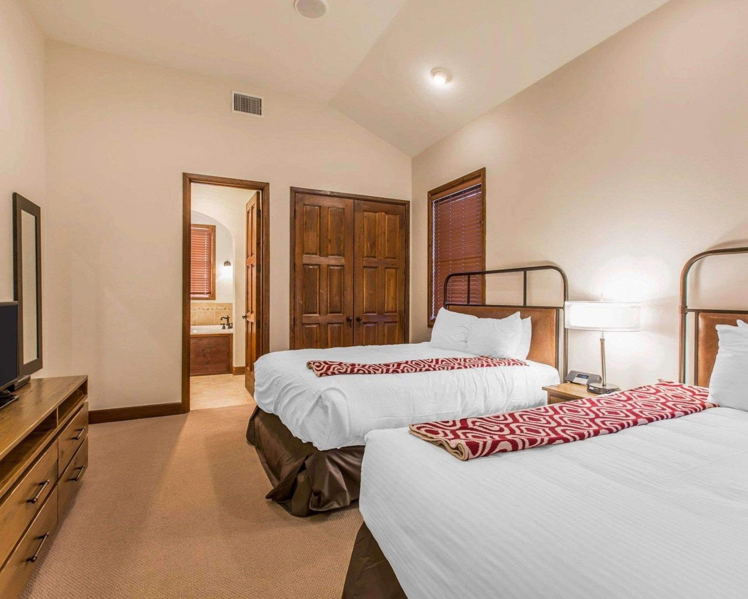 Habitación de hotel con dos camas, un armario de madera, un baño con ducha y un televisor sobre un aparador de madera.