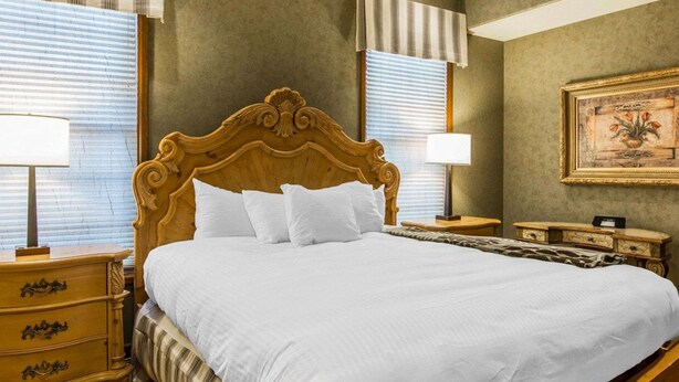 A large bed with a wooden headboard, two bedside tables with lamps, a nightstand with a lamp, and a framed picture on the wall.