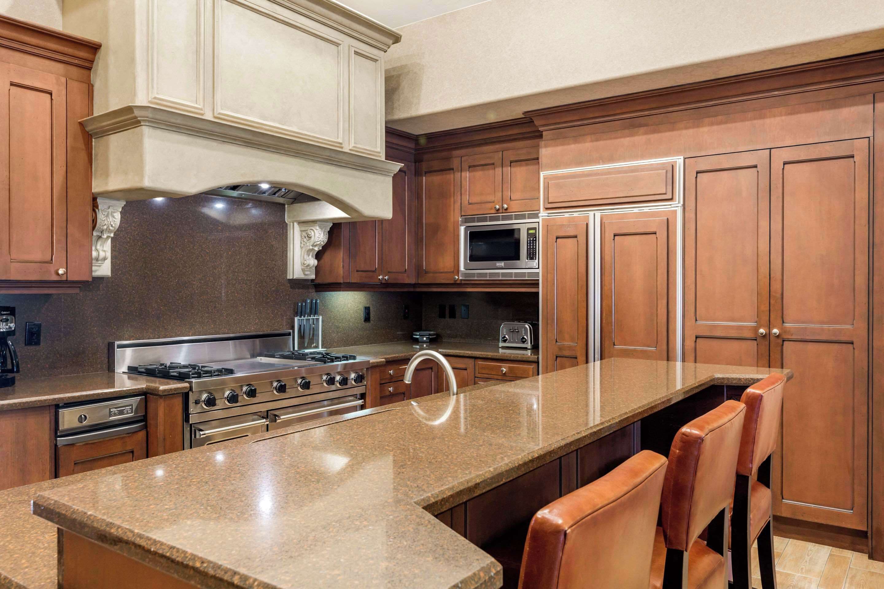 A kitchen with granite countertops, stainless steel appliances, wooden cabinets, and a central island with bar stools.