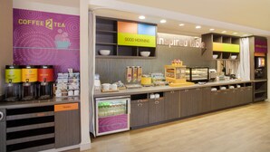A coffee and tea station with dispensers, a refrigerator, and a counter with bowls and trays. - Home2 Suites by Hilton Charlotte I-77 Tyvola Rd (Charlotte)