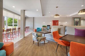 A modern lounge area with a sofa, chairs, and a table. There are large windows providing a view of the outdoors.
