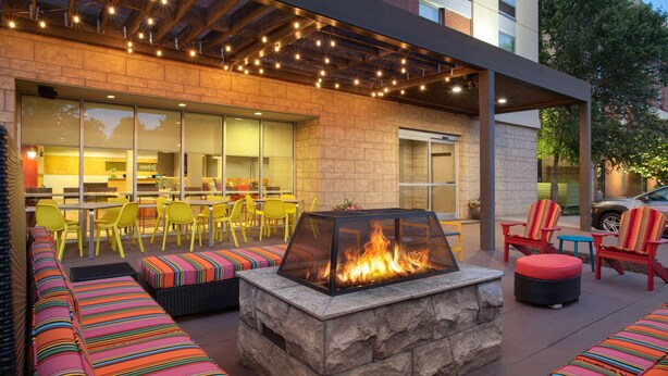 An outdoor seating area with a stone fire pit, yellow chairs, and colorful striped cushions. - Home2 Suites by Hilton Charlotte I-77 Tyvola Rd (Charlotte)