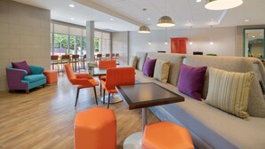 A modern lounge area with a sofa, orange chairs, and a table. - Home2 Suites by Hilton Charlotte I-77 Tyvola Rd (Charlotte)