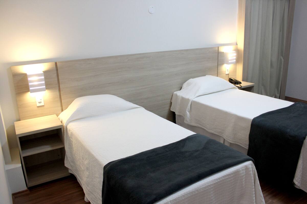 Een hotelkamer met twee eenpersoonsbedden, elk voorzien van een nachtkastje en lamp.