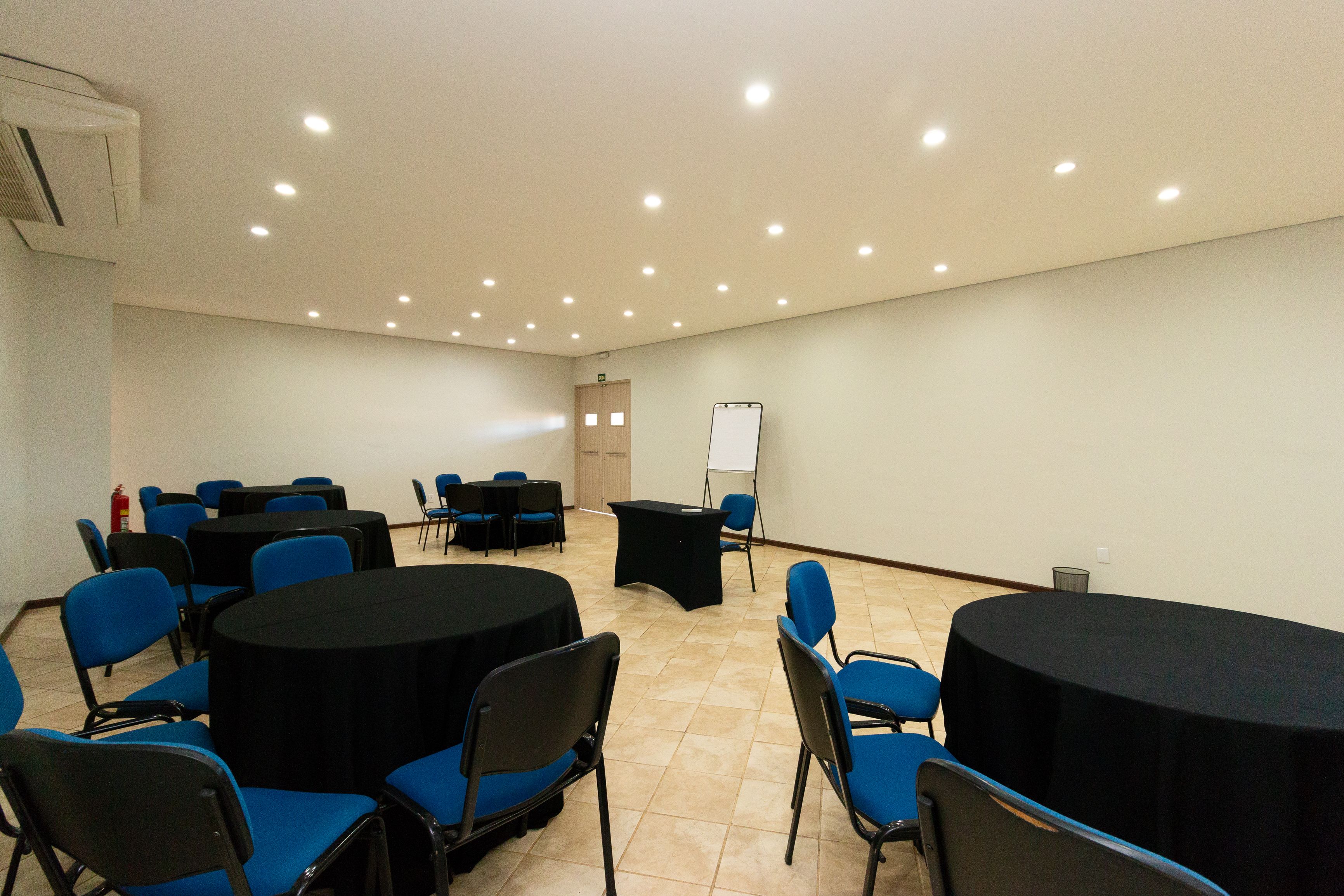 Ein Konferenzraum mit runden Tischen, blauen Stühlen, einer Tafel und einem schwarzen Rednerpult.