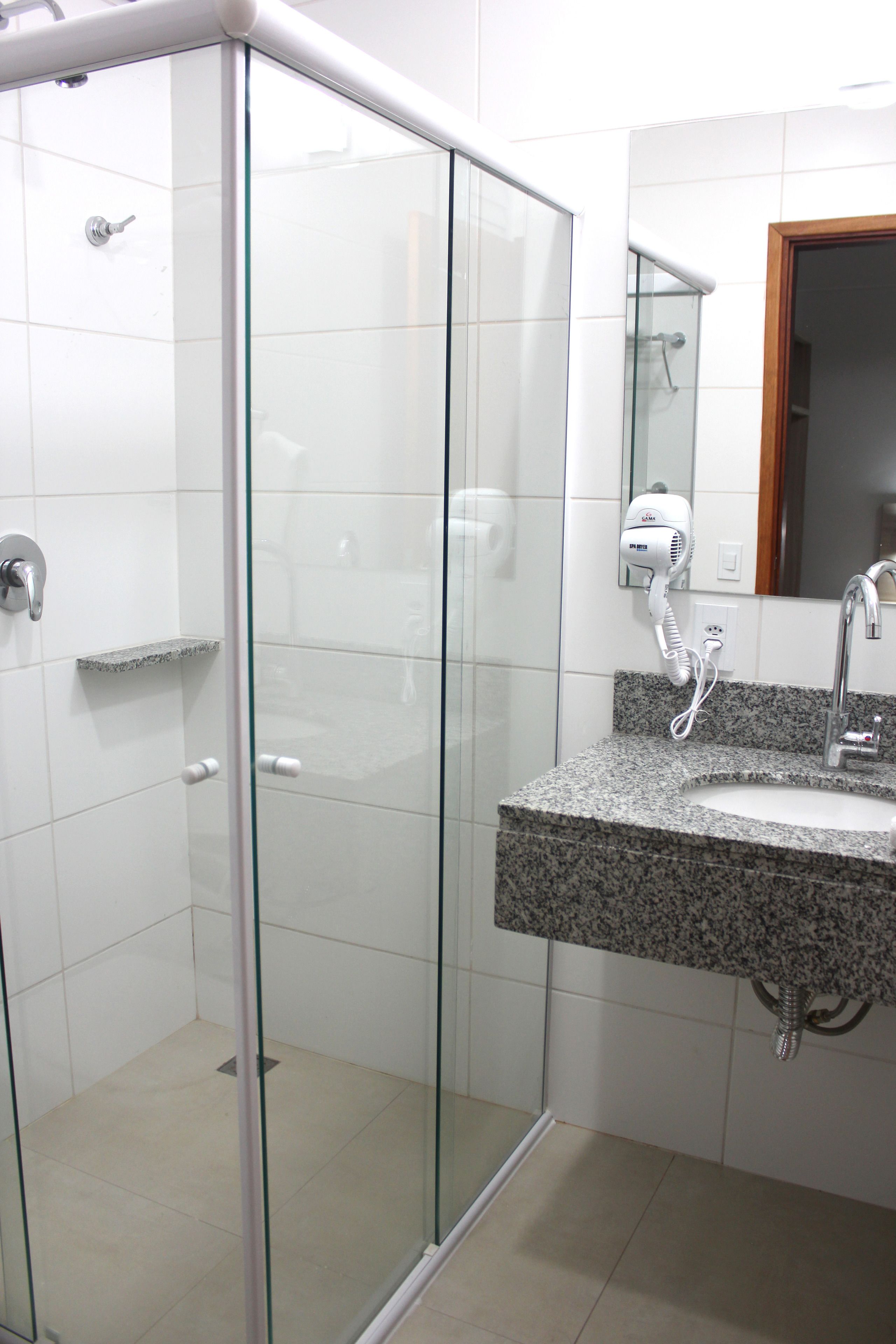 Un baño moderno con ducha envuelta en vidrio, lavamanos con encimera de granito y espejo sobre el lavamanos.