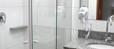 Un baño moderno con ducha envuelta en vidrio, lavamanos con encimera de granito y espejo sobre el lavamanos.