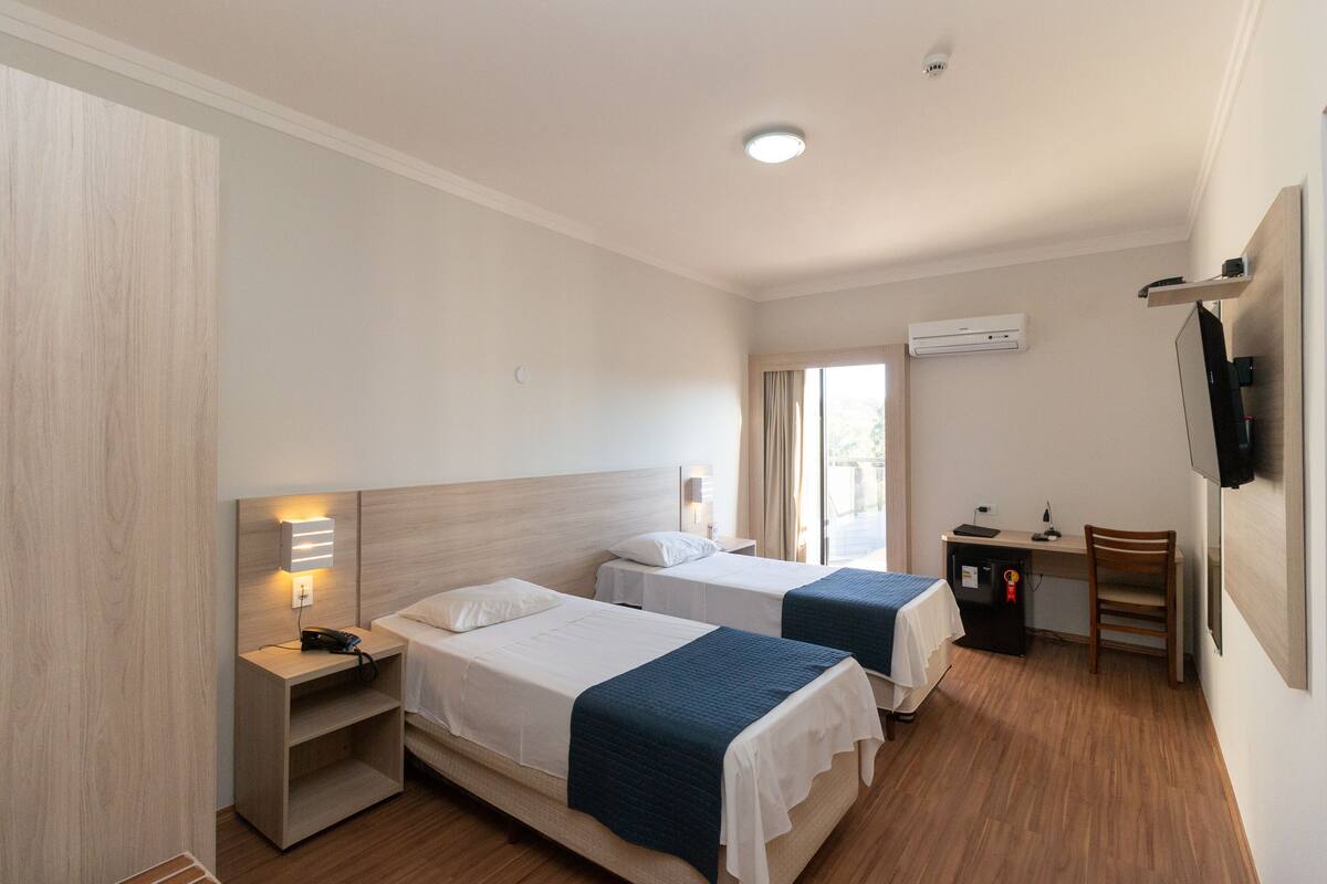 Een hotelkamer met twee bedden, een bureau, een stoel, een televisie en een airconditioning.
