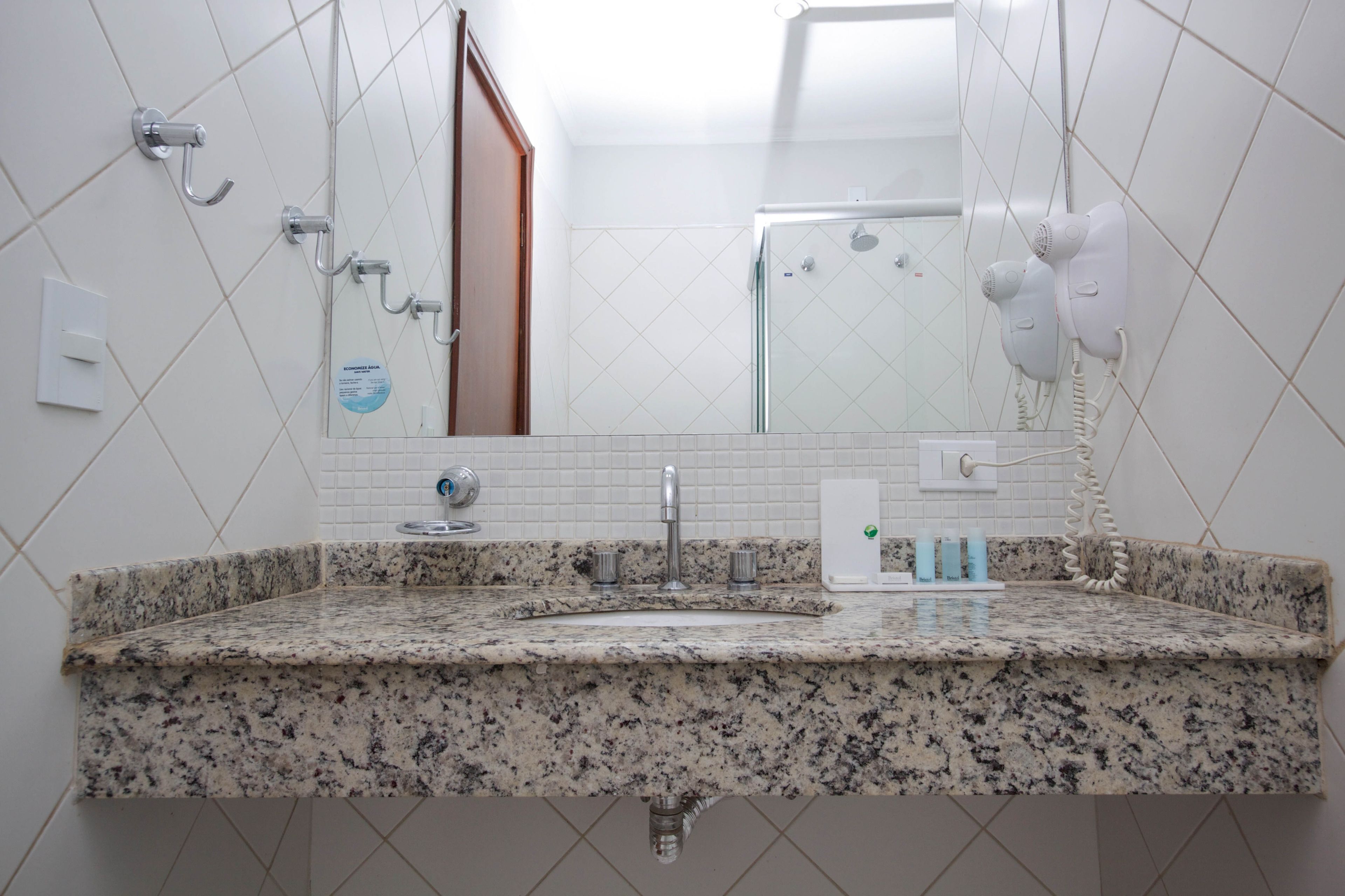 Une salle de bain avec un comptoir en granit, un lavabo, un miroir, une douche et un sèche-cheveux.