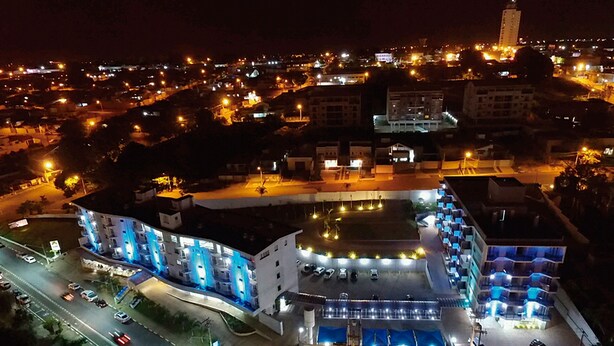 Vue aérienne d’un hôtel à plusieurs étages, avec un parking et un environnement urbain environnant, le tout illuminé la nuit.