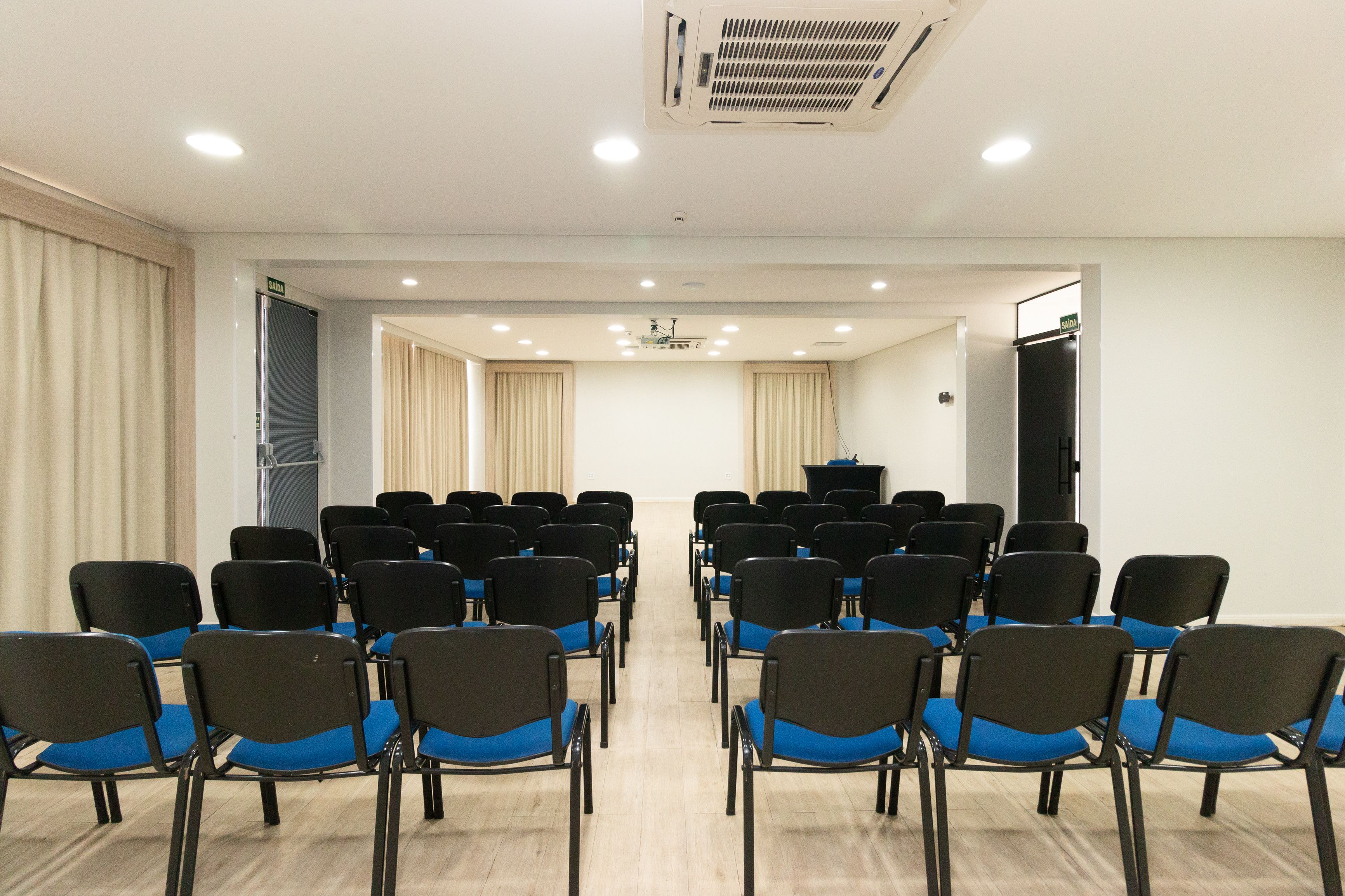 A conference room with rows of chairs, a podium, and a projector screen.