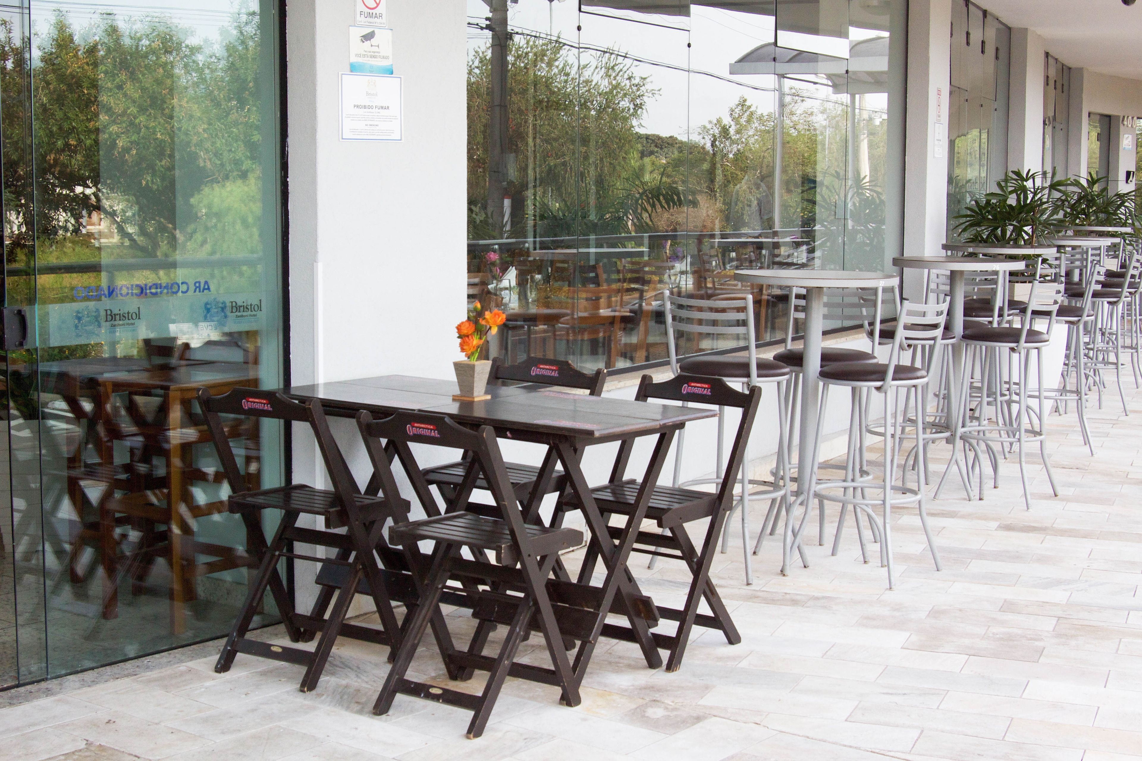 Un espace café en plein air avec des tables et des chaises, un mur en verre et des plantes en pot.