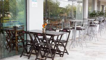 Un espace café en plein air avec des tables et des chaises, un mur en verre et des plantes en pot.