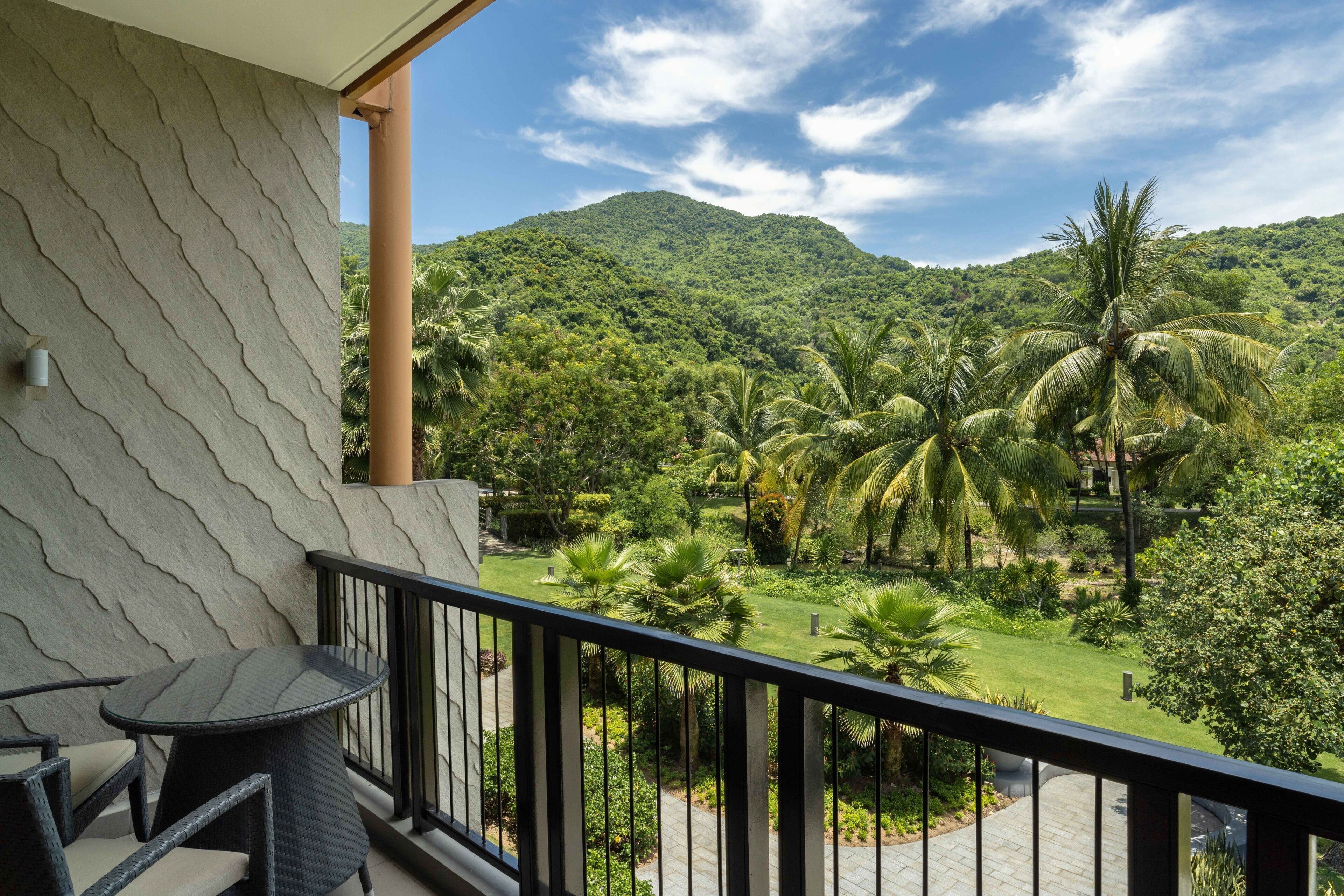 A balcony with a view of a lush garden and a mountain.