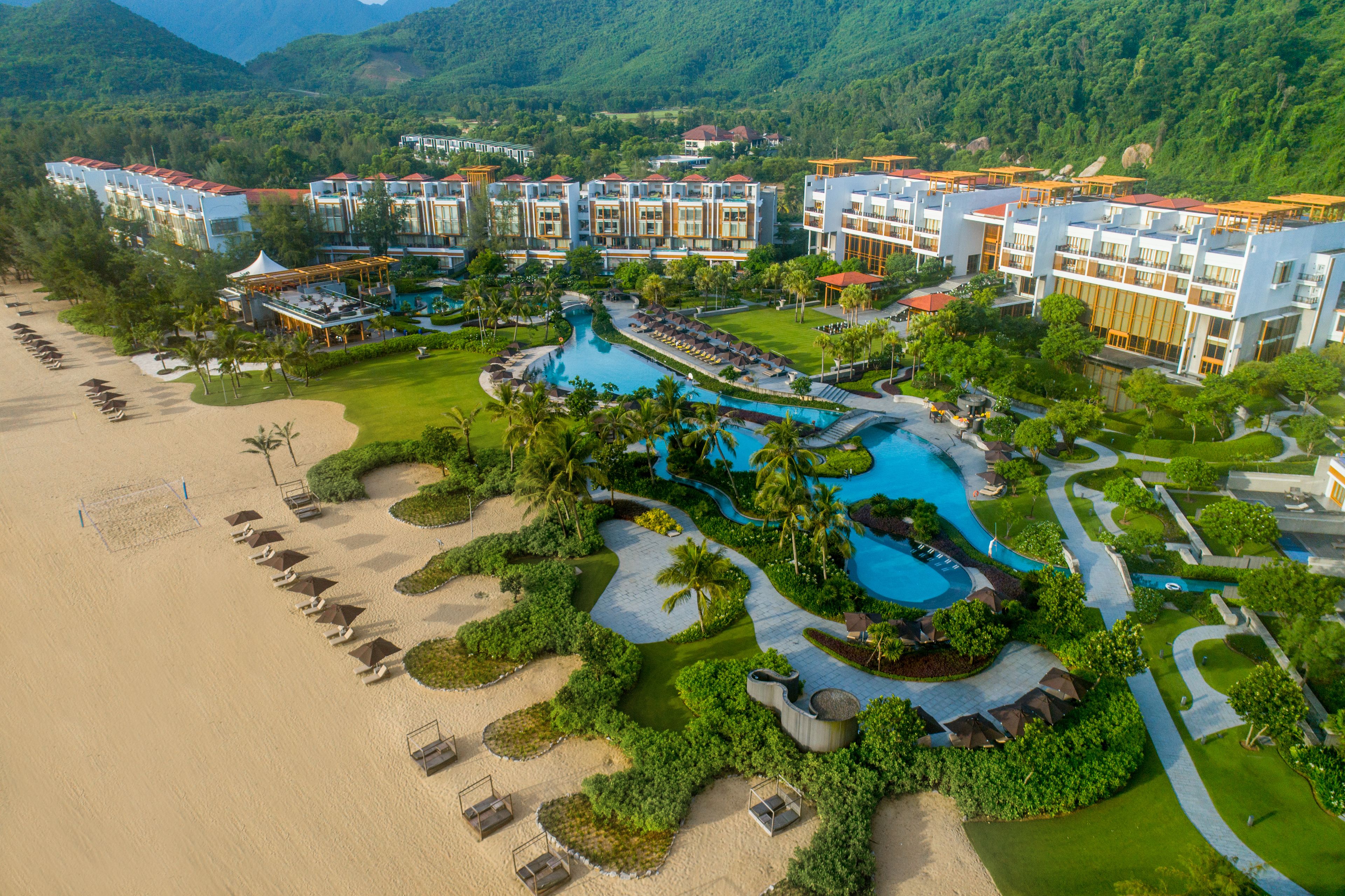 A resort with multiple buildings, a large swimming pool, and a beach area.