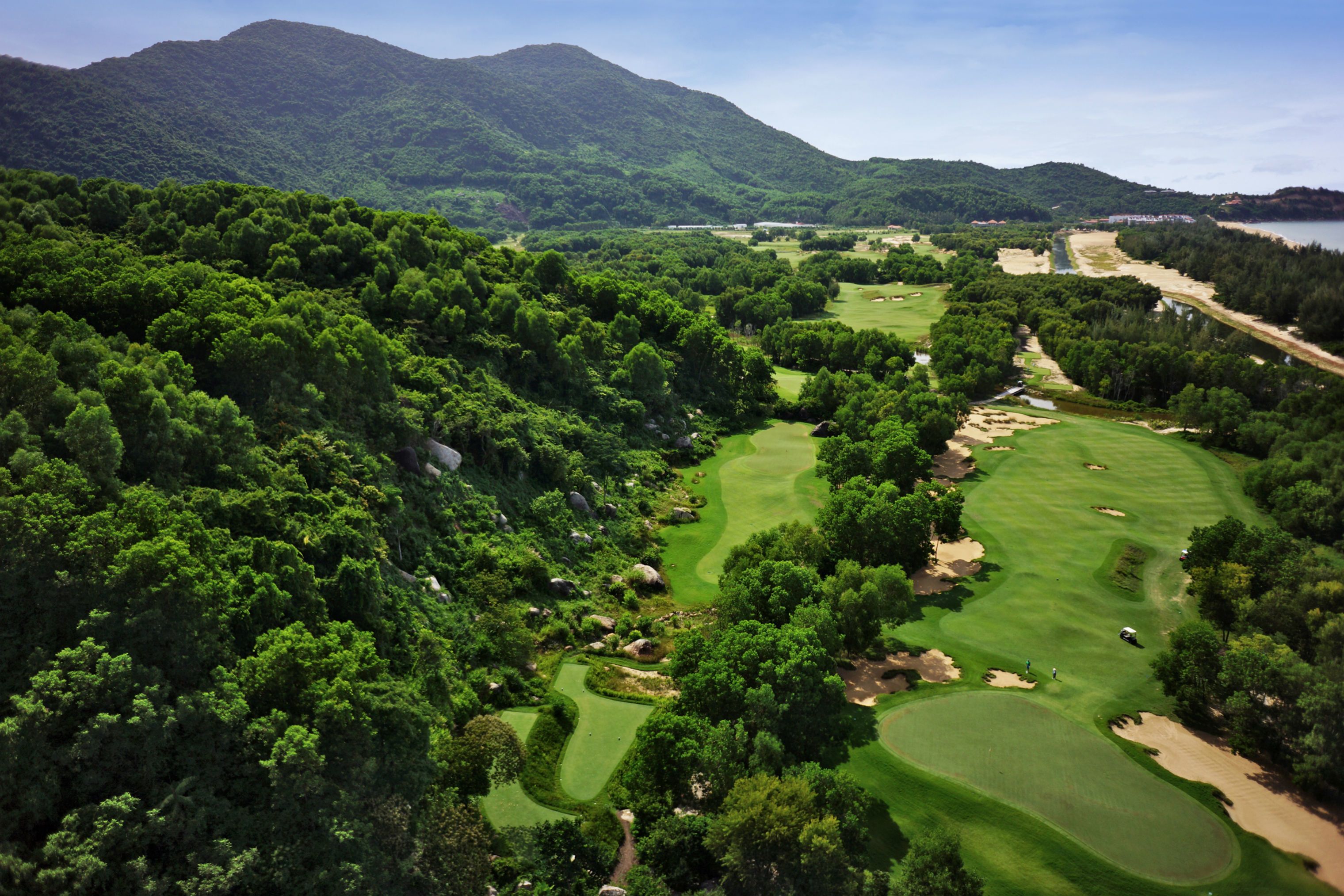 A golf course with lush greenery and a mountainous backdrop.