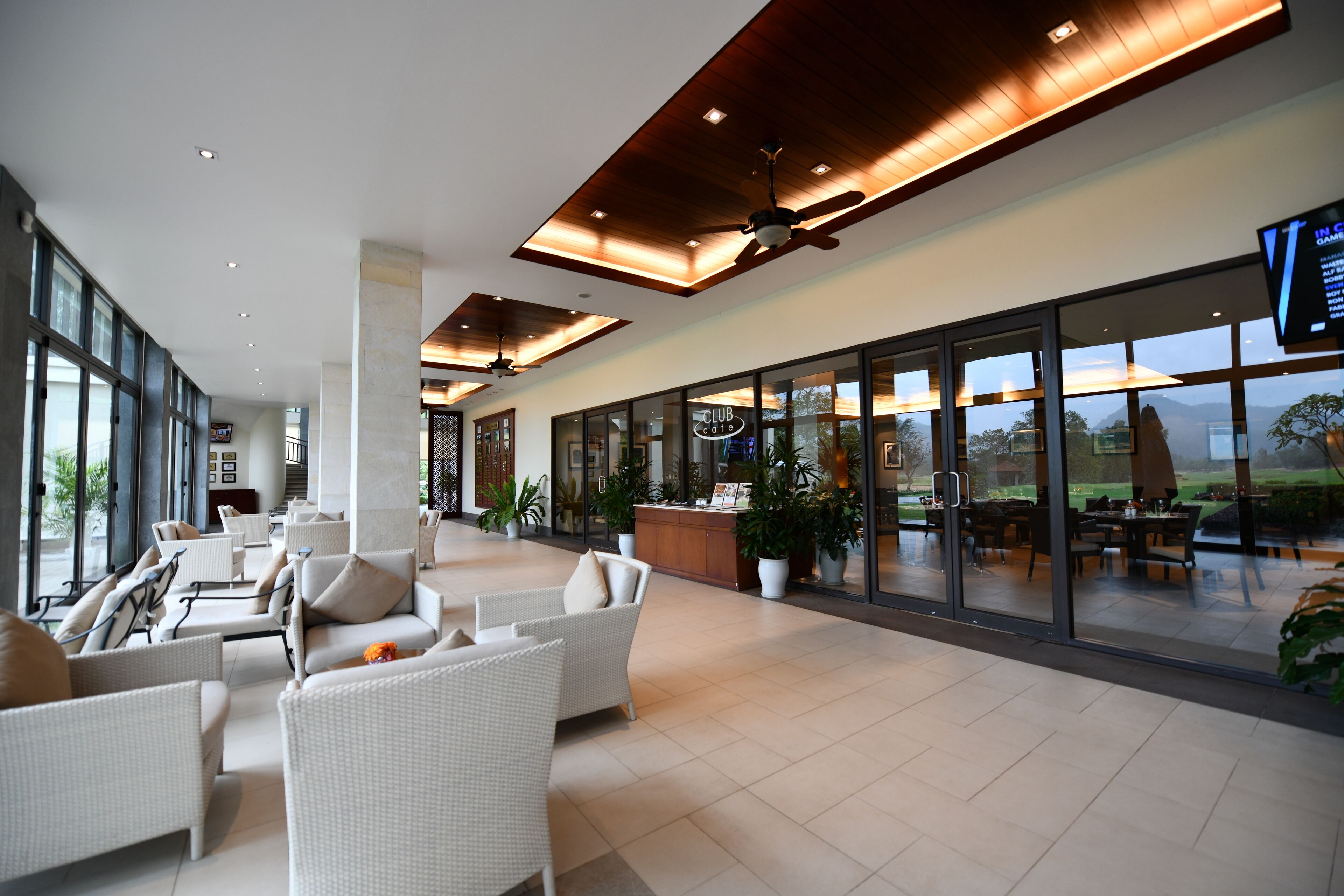 A spacious indoor area with wicker furniture, a ceiling fan, and large windows offering a view of the outdoors.
