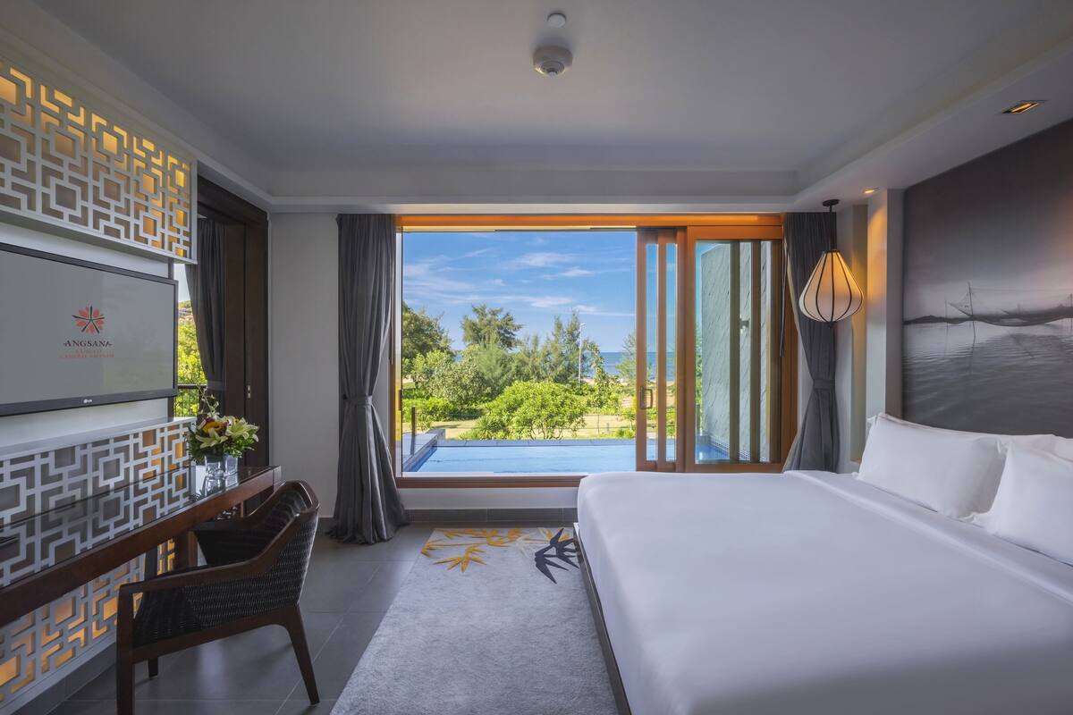 A hotel room with a large bed, a desk with a chair, a TV, and a view of the outdoors.