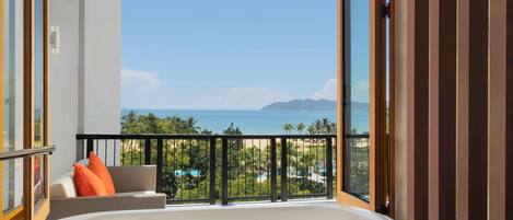 A balcony with a view of the sea, a bathtub, and a sofa with orange cushions.