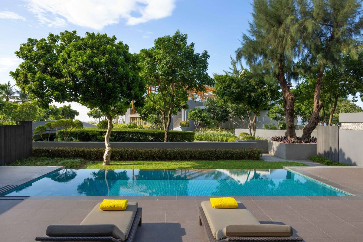 A swimming pool with two sun loungers, surrounded by trees and a well-maintained garden.