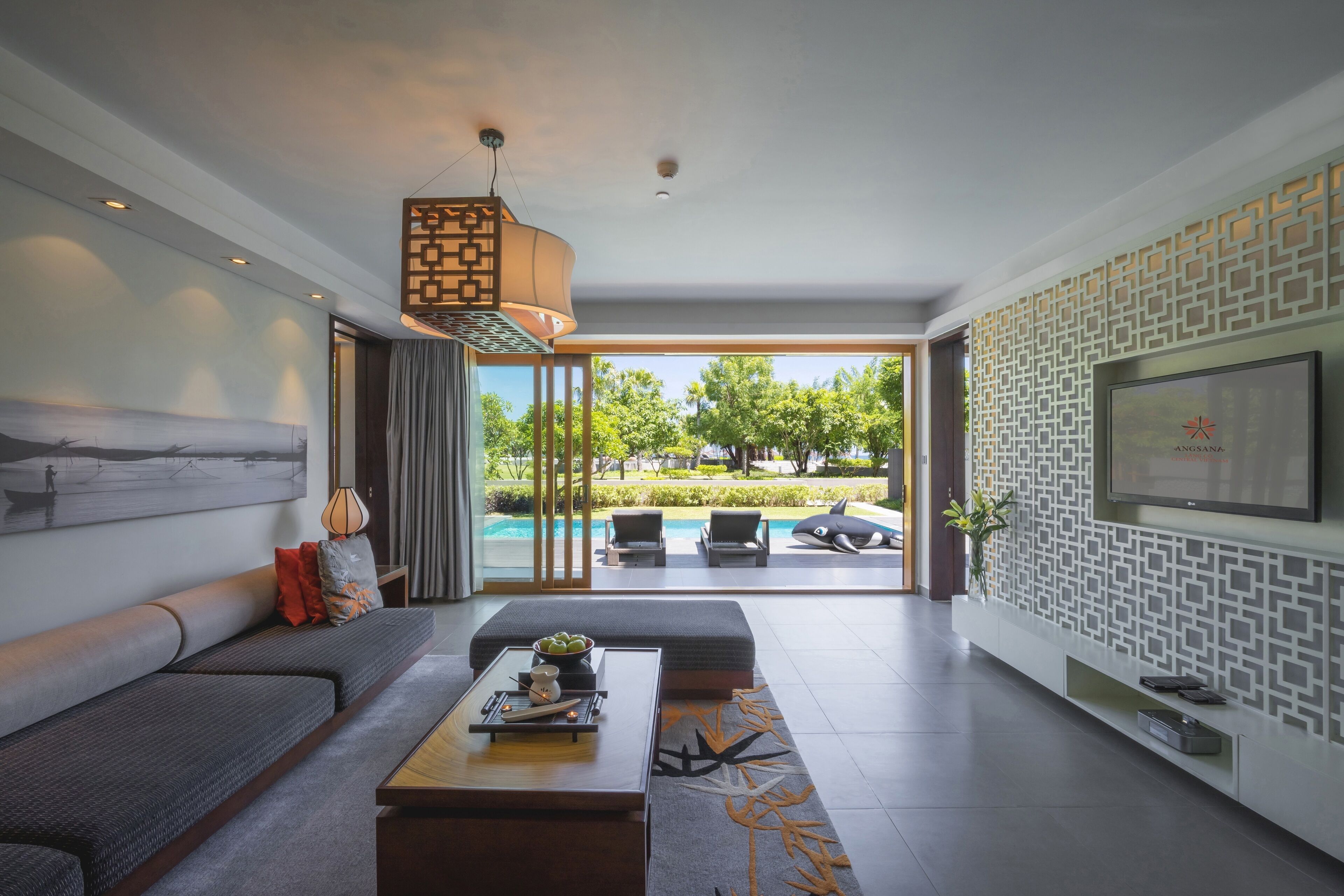 A modern living room with a sofa, coffee table, and a view of a swimming pool.