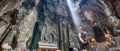 A cave temple with a central shrine, stone carvings, and a small building with a tiled roof.