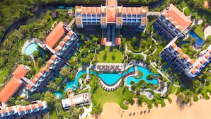 Vue aérienne d’un complexe hôtelier comprenant plusieurs bâtiments, une piscine centrale et une zone de plage.