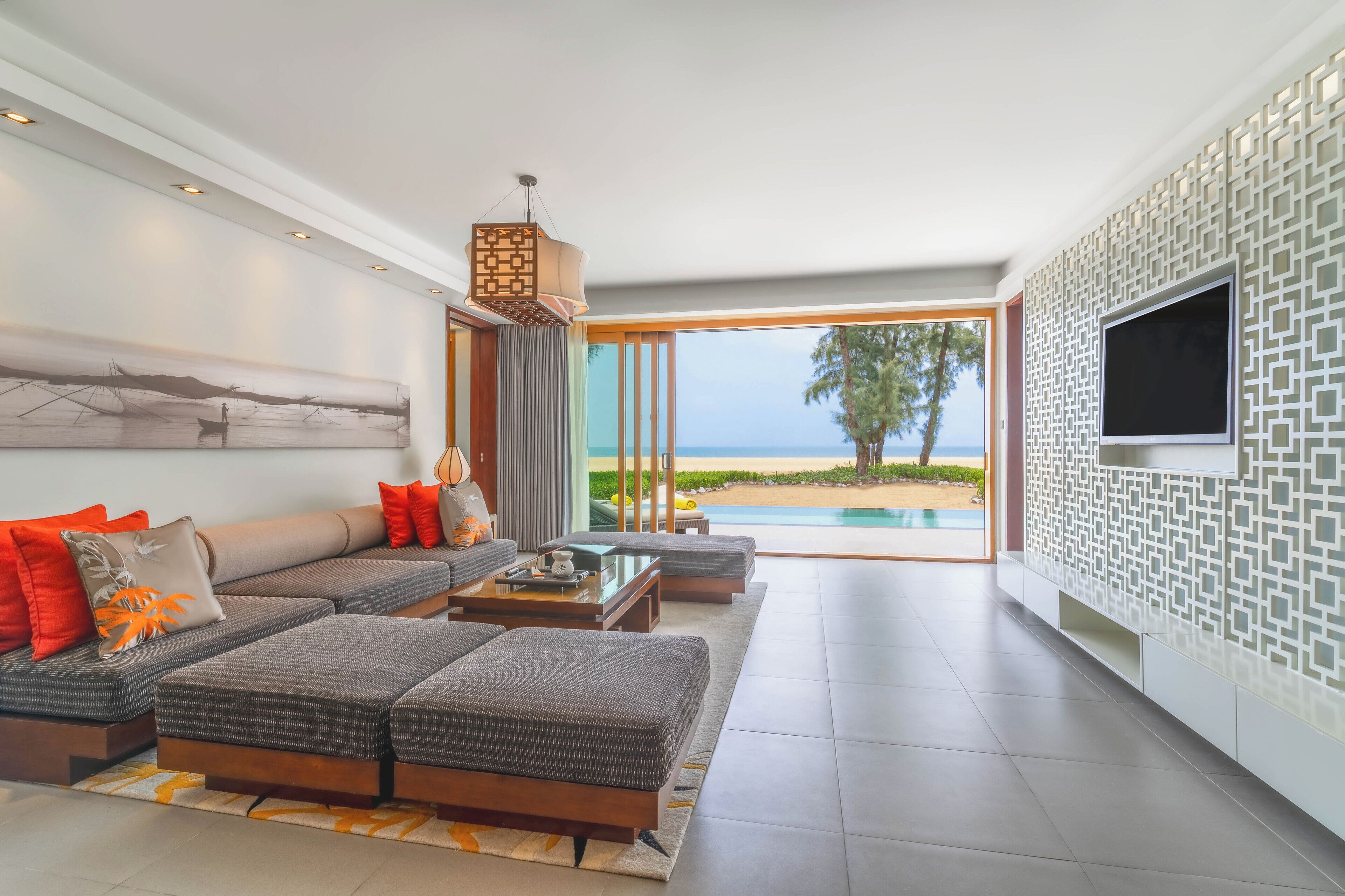 A modern living room with a large sofa, a coffee table, and a TV. There is a view of the ocean through large windows.