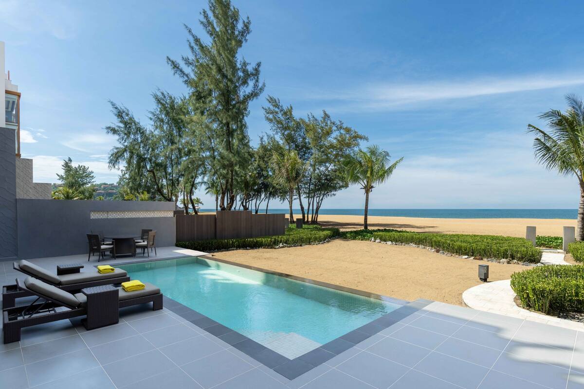 A modern outdoor pool area with lounge chairs, a table, and a view of the beach and ocean.