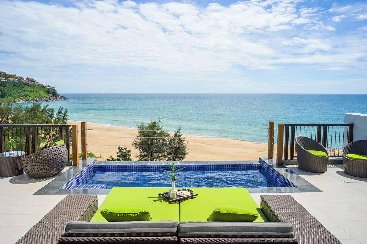 A pool area with a view of the beach and ocean, surrounded by wicker furniture and a tiled deck.