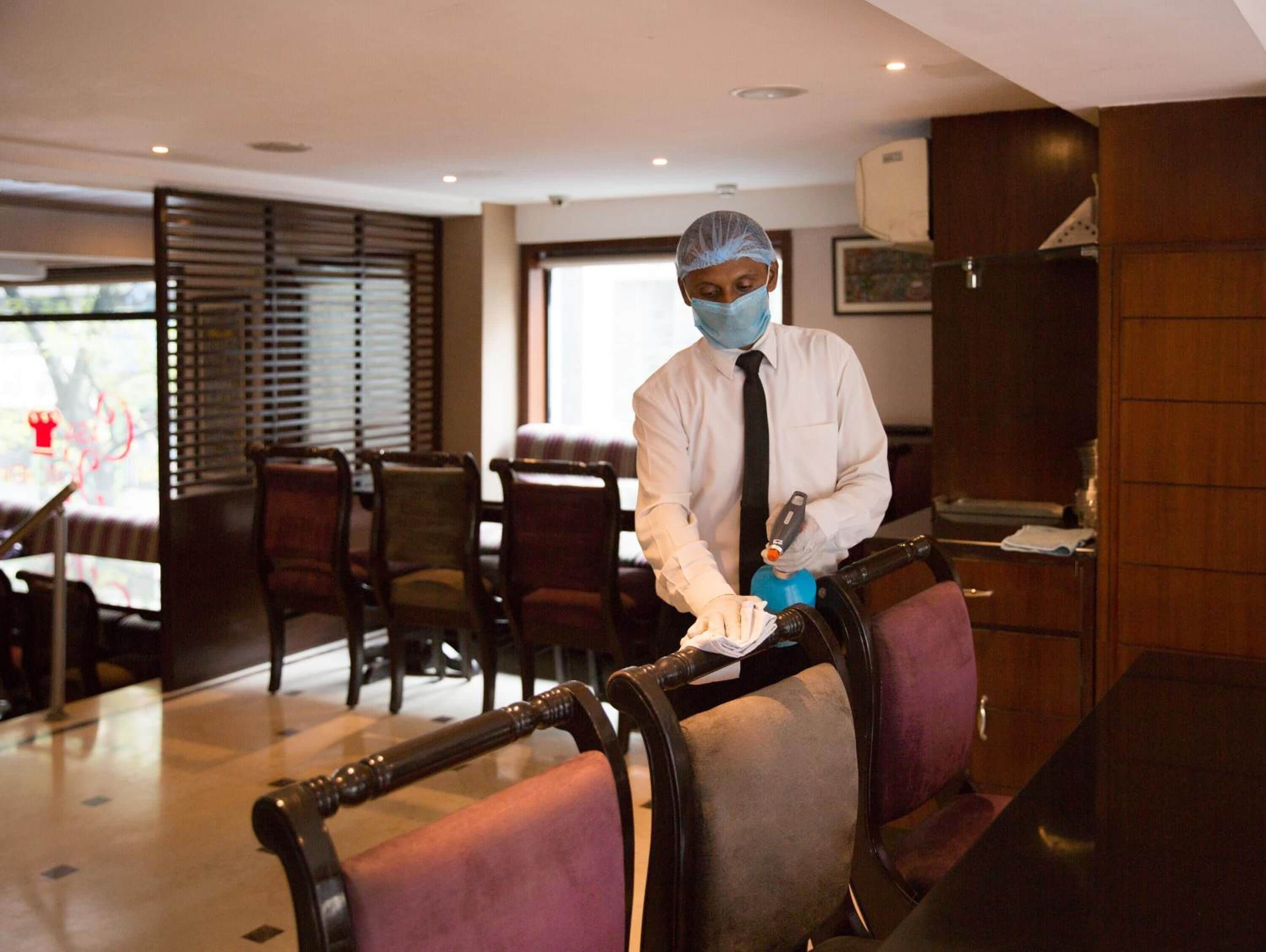 A person cleaning a chair in a hotel room with wooden furniture and a window with blinds.