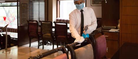 A person cleaning a chair in a hotel room with wooden furniture and a window with blinds.