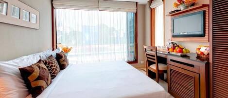 Habitación de hotel con una cama grande, un escritorio con televisor de pantalla plana y vistas a la ciudad a través de cortinas translúcidas.