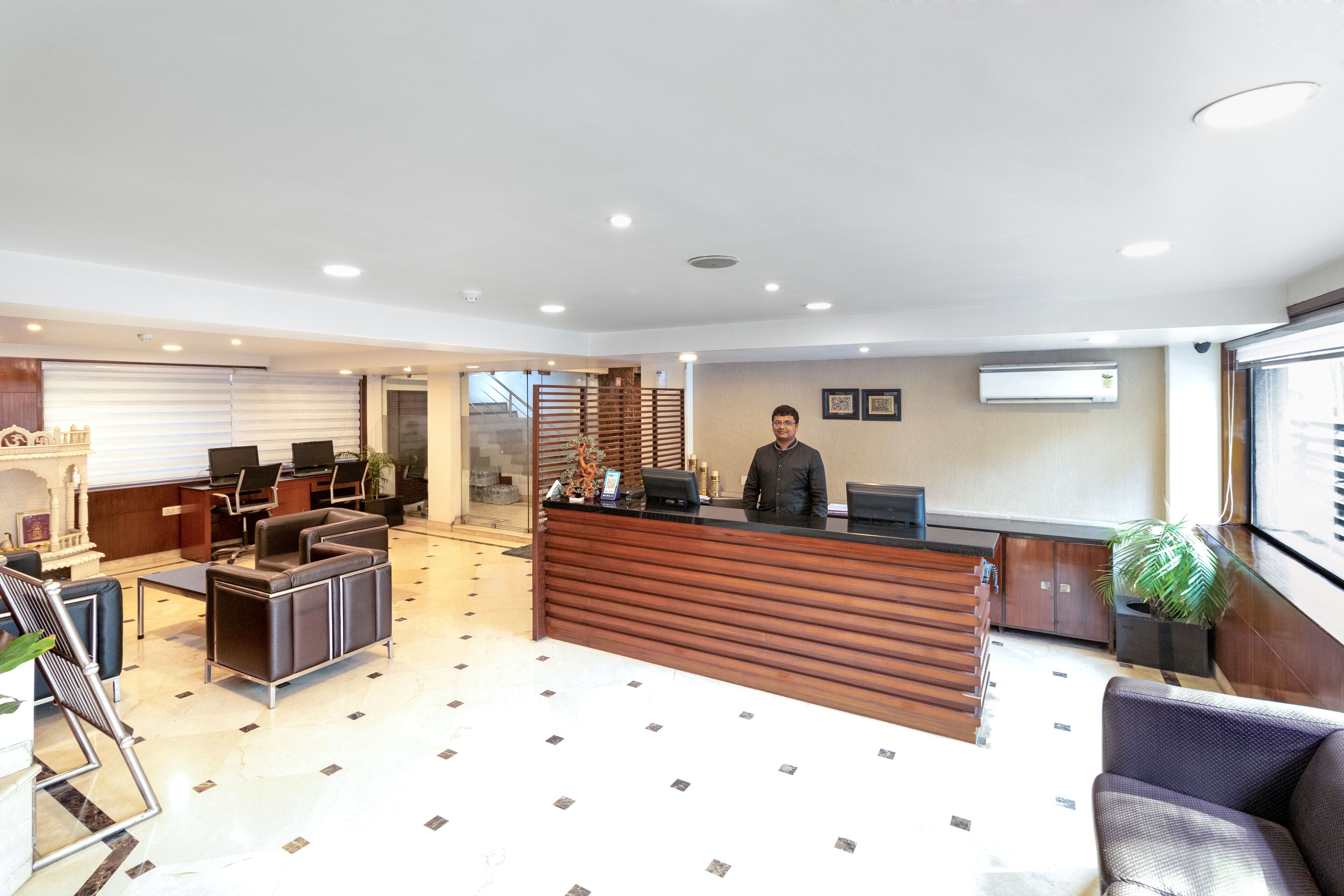 A modern hotel lobby with a reception desk, seating area, and a staircase leading to an upper floor.