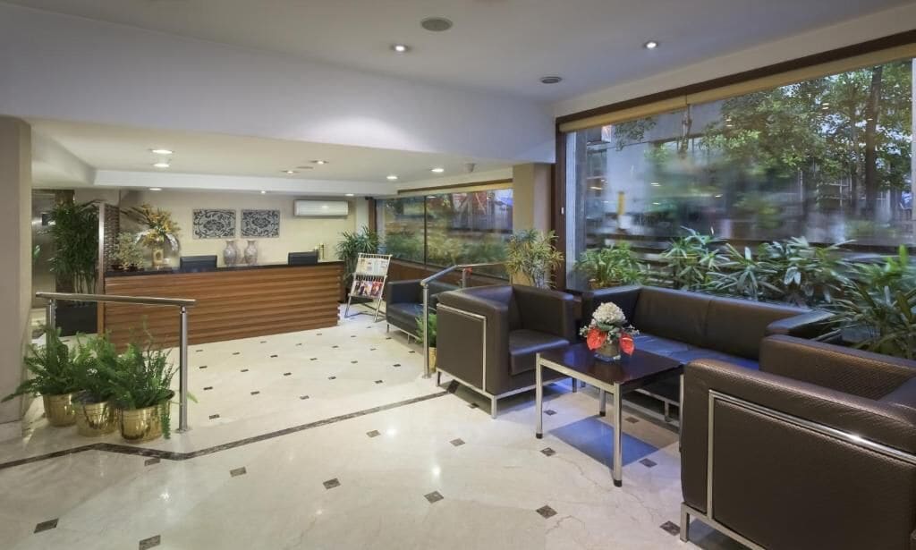 A modern lobby with a reception desk, seating area, and large windows overlooking a garden.