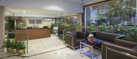 A modern lobby with a reception desk, seating area, and large windows overlooking a garden.
