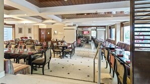 A spacious dining area with multiple tables and chairs, wooden ceiling beams, and large windows allowing natural light. - Hotel Casa Fortuna (Kolkata)