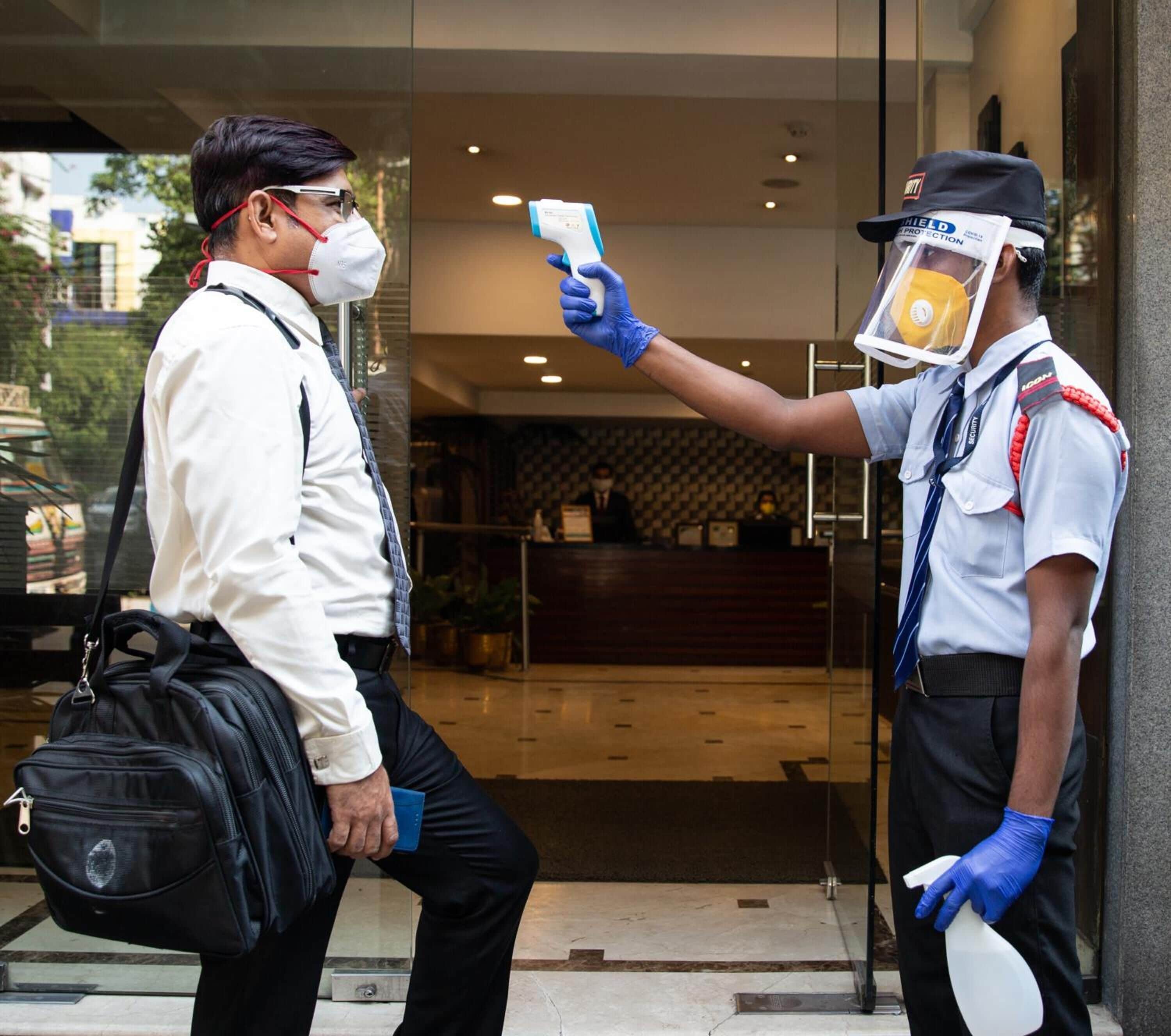 A security guard conducting a temperature check on a person entering a building.