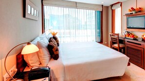 A hotel room with a large bed, a desk with a lamp, a television, and a view of the outside through the window. - Hotel Casa Fortuna (Kolkata)