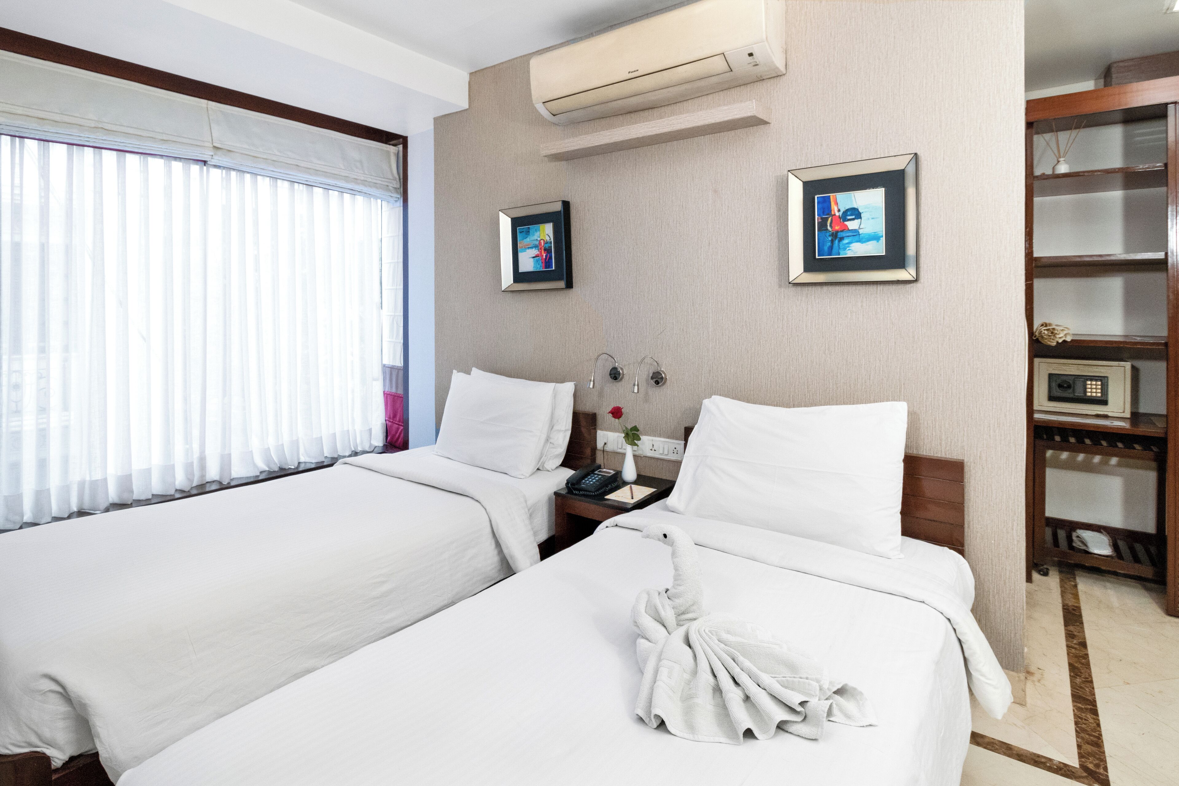 A hotel room with two beds, a bedside table with a phone and a vase, and a wall-mounted air conditioner.