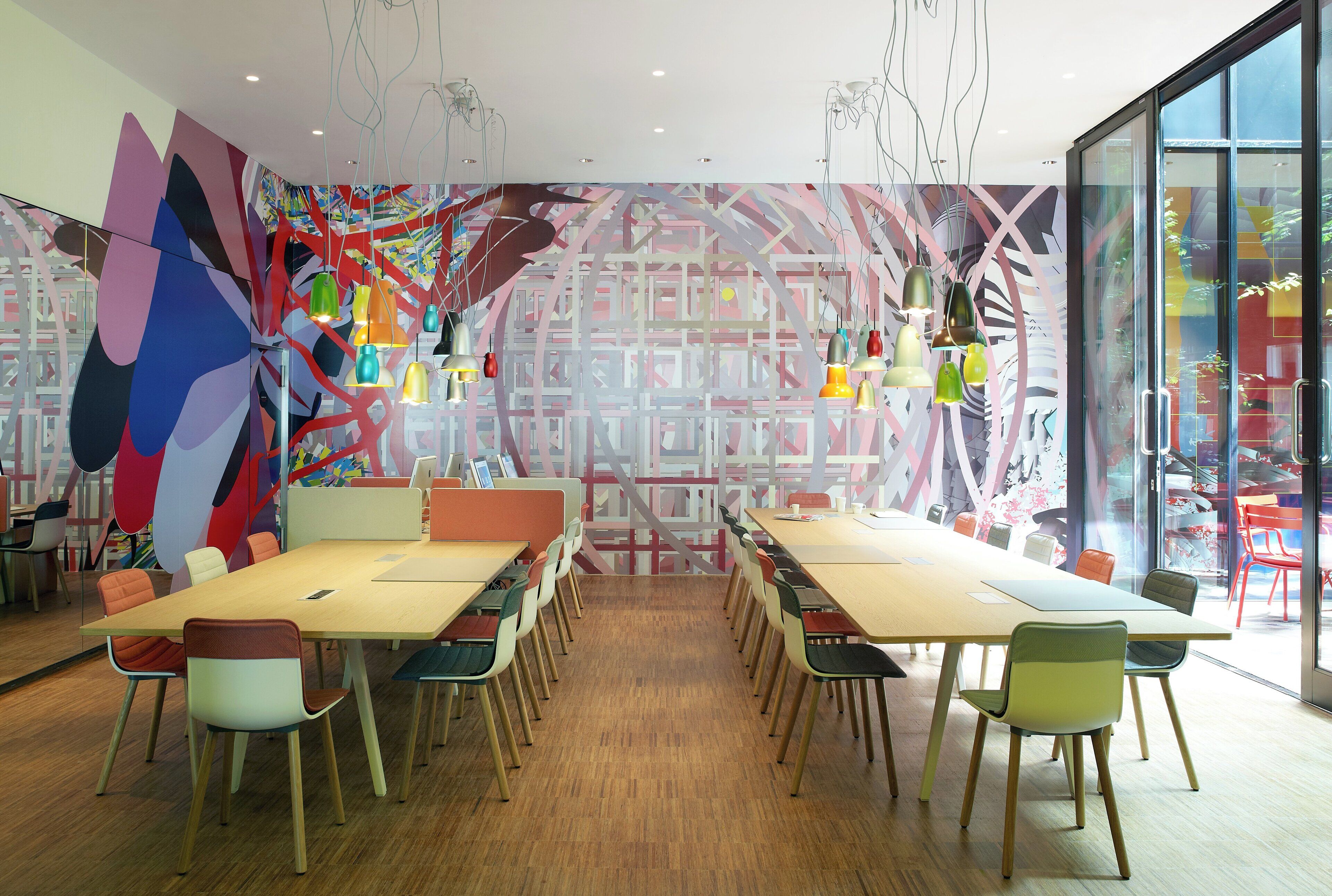 Una sala de reuniones moderna con una mesa grande, sillas coloridas y arte abstracto en las paredes.