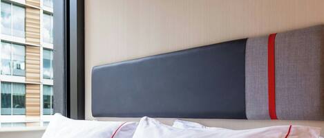 Ein Hotelzimmer mit einem ordentlich bezogenen Bett, einem großen Fenster und einem modernen Kopfschild.